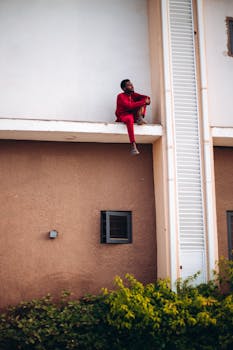 Man in red outfit sitting on building ledge, showcasing urban adventure and boldness.