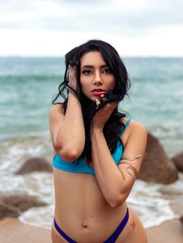 Model in a blue bikini posing confidently by the ocean shore.