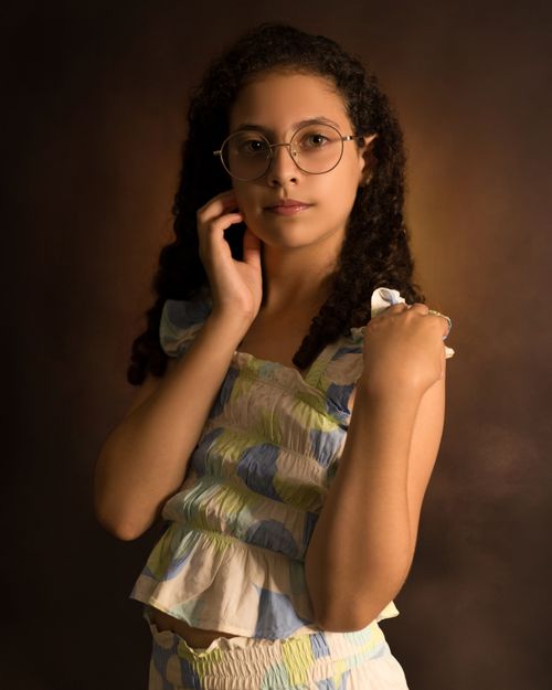 Free A young girl wearing glasses poses elegantly in a studio with soft lighting. Stock Photo