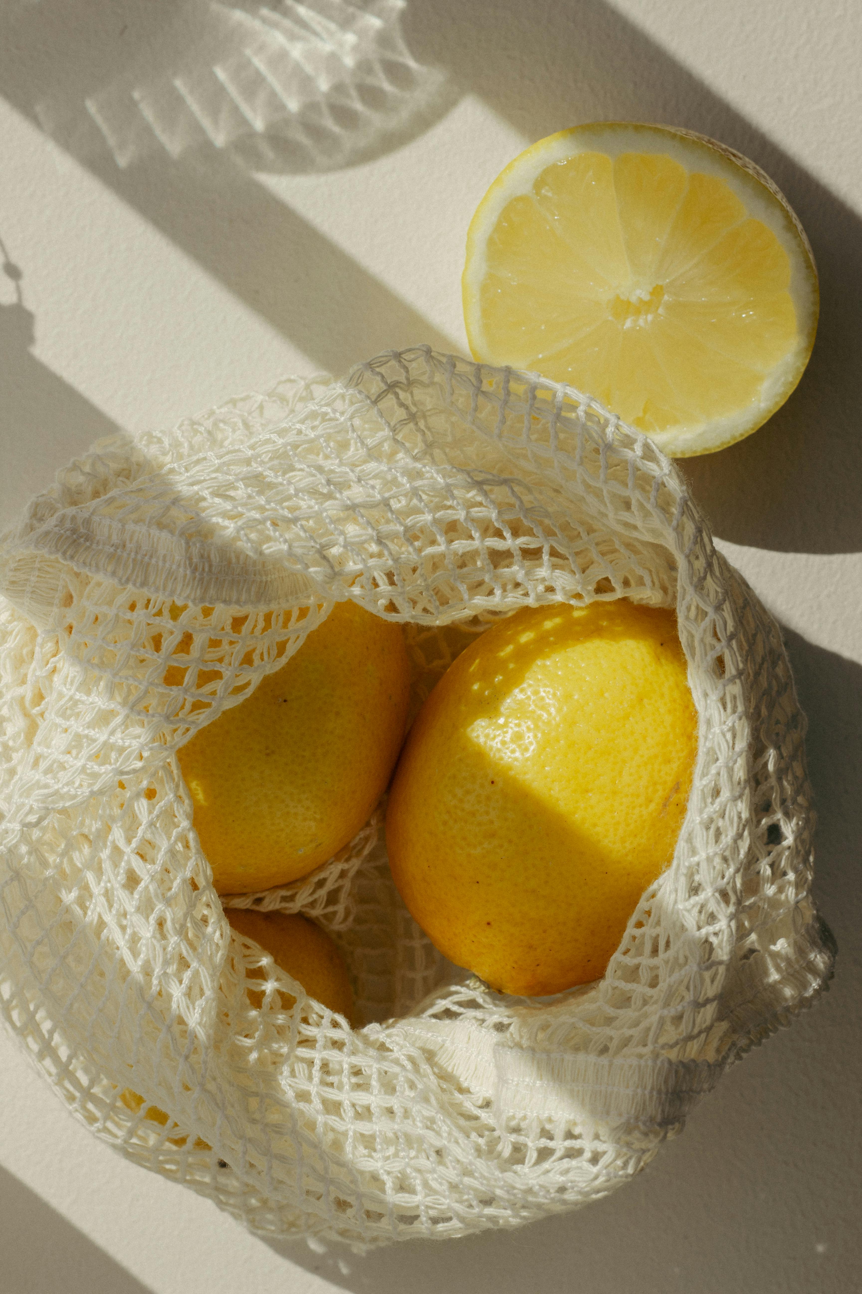 Bright yellow lemons in a net bag with dramatic shadows from sunlight.