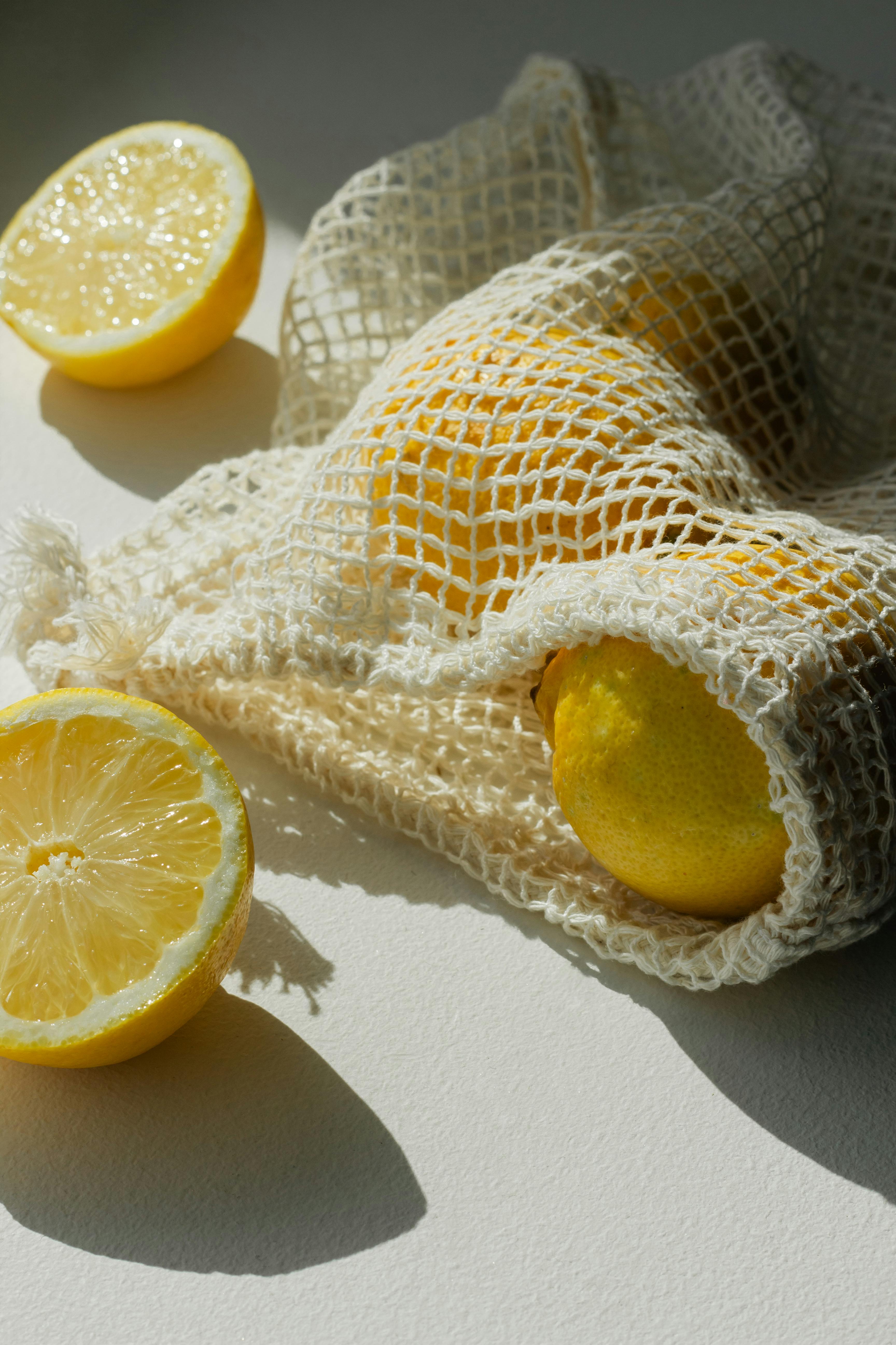 Sunny and fresh lemons spilling from an eco-friendly mesh bag, casting soft shadows on a white surface.