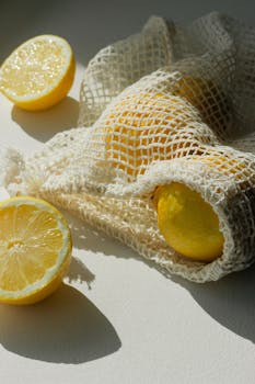 Sunny and fresh lemons spilling from an eco-friendly mesh bag, casting soft shadows on a white surface.