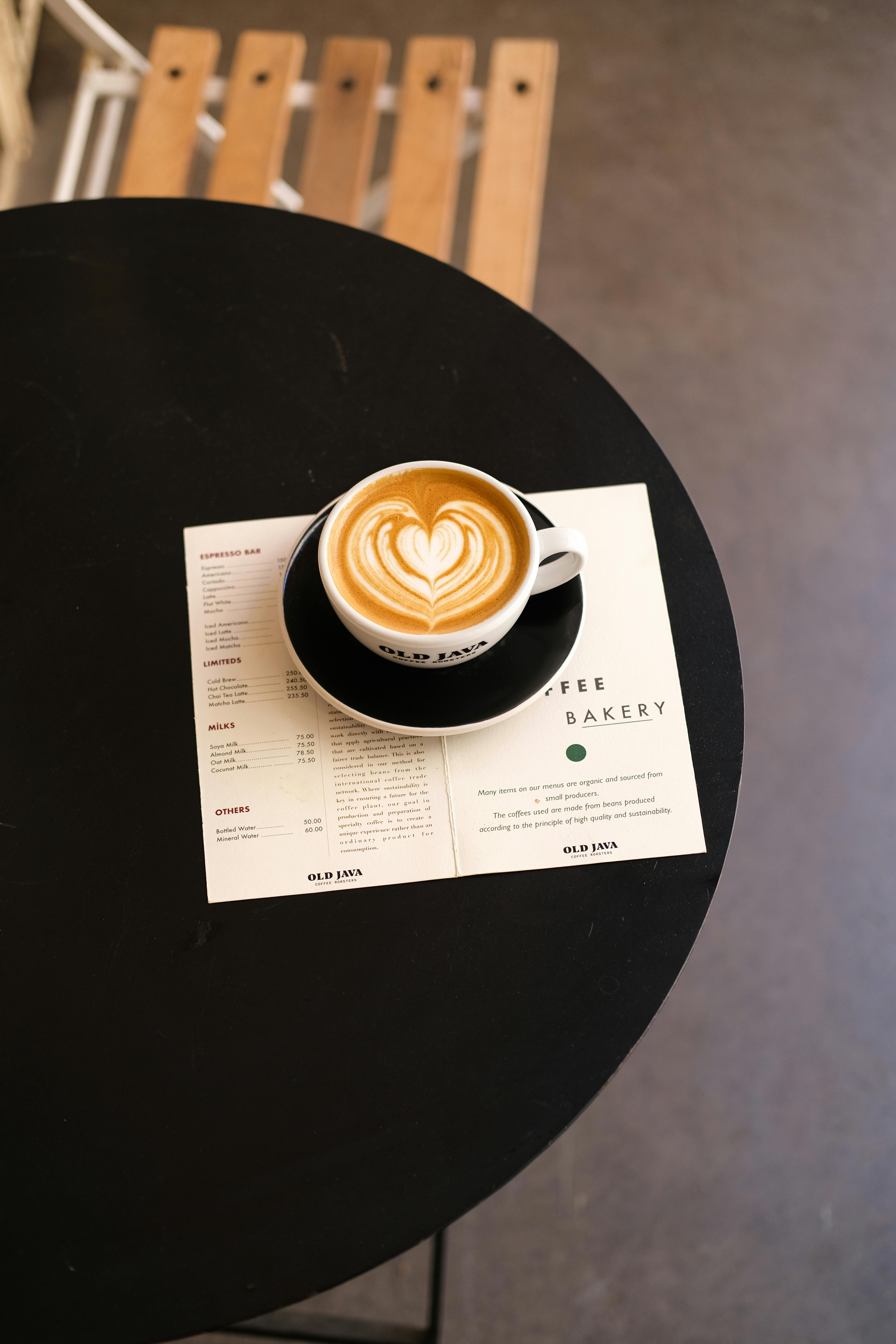 Top view of a latte with heart-shaped art served on a black table alongside a cafe menu.