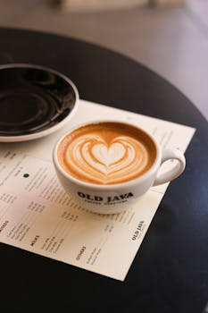 A cup of latte with heart-shaped design at Old Java cafe, set on a menu.