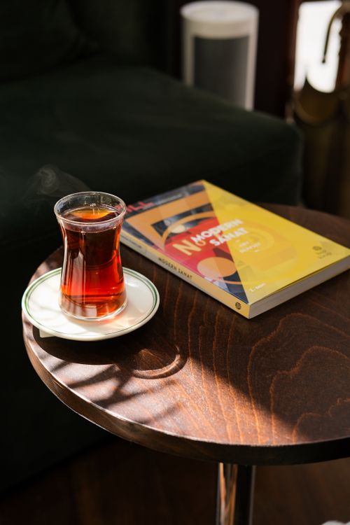 Free Cozy scene with a steaming tea glass and a book on a wooden table, sunlight streaming in. Stock Photo