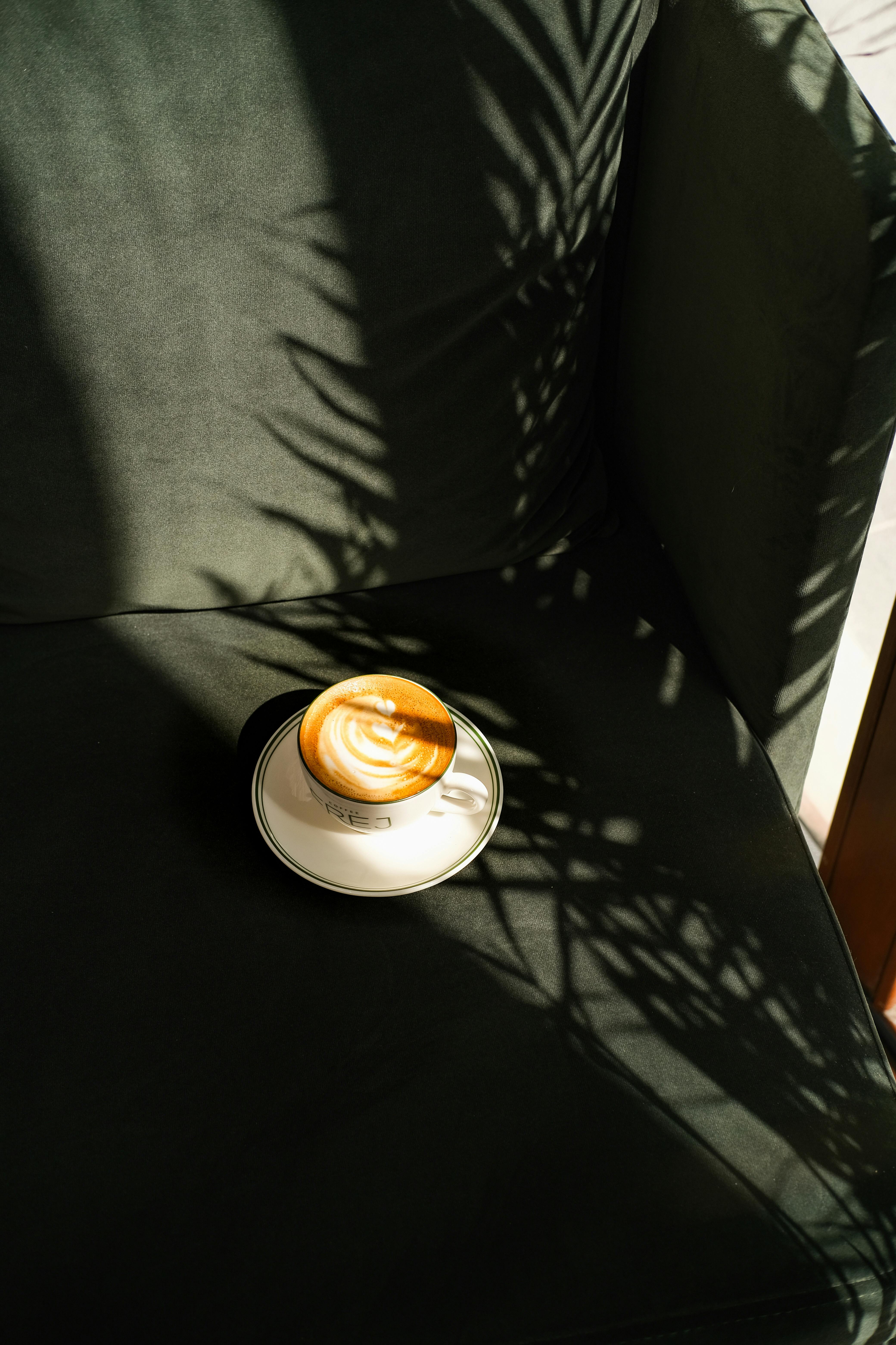 A stylish cup of cappuccino on a green sofa, highlighted by artistic shadows and sunlight.