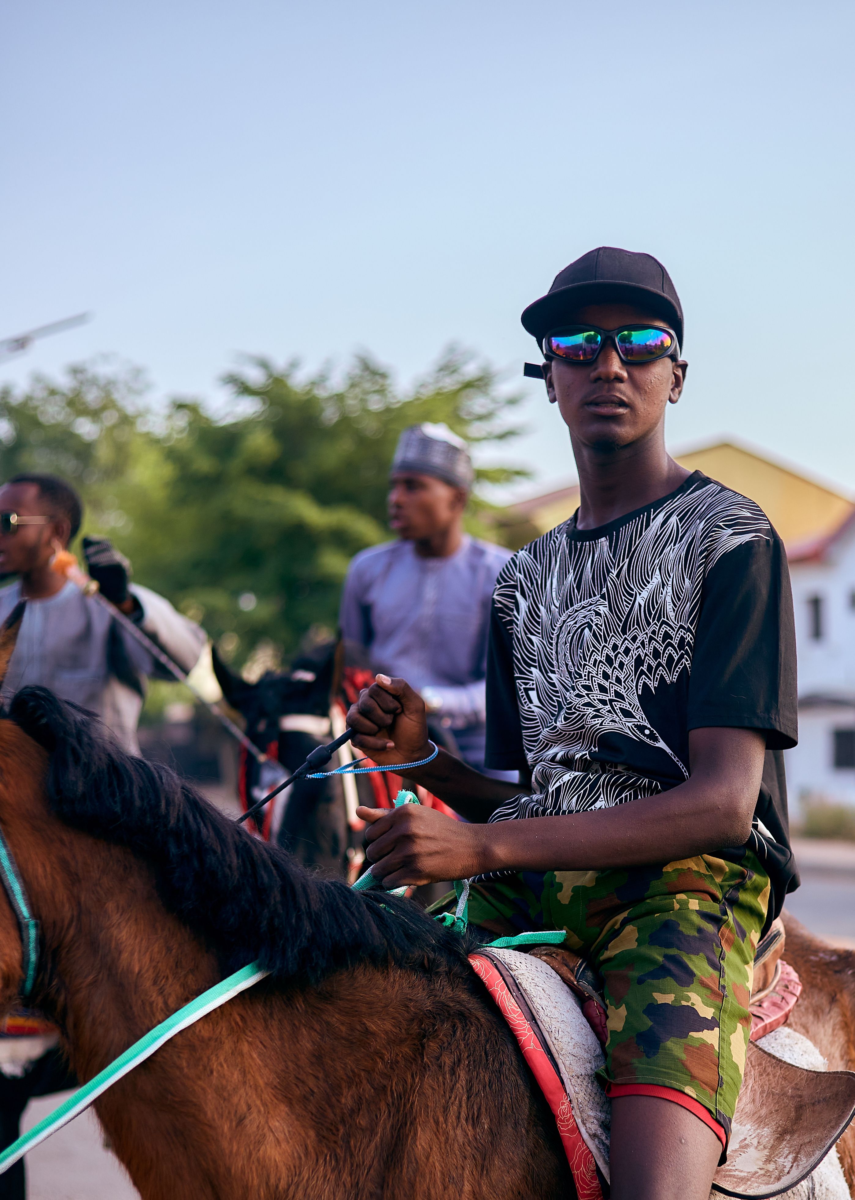 A young man in sunglasses and casual attire rides a horse outdoors, exuding a sense of adventure.
