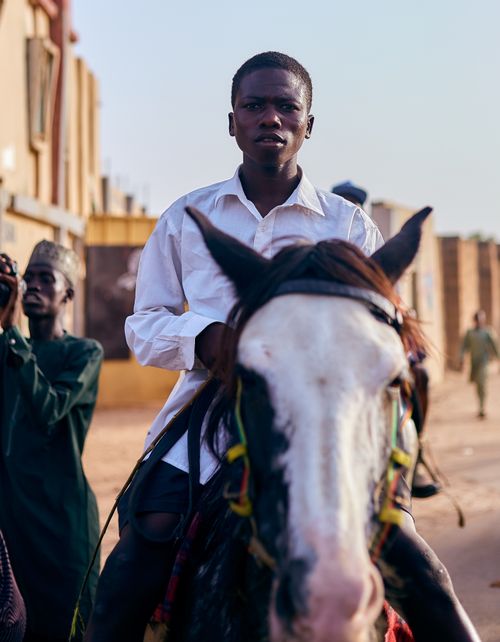 Free A young man rides a horse on a city street, capturing a vibrant moment of urban life. Stock Photo