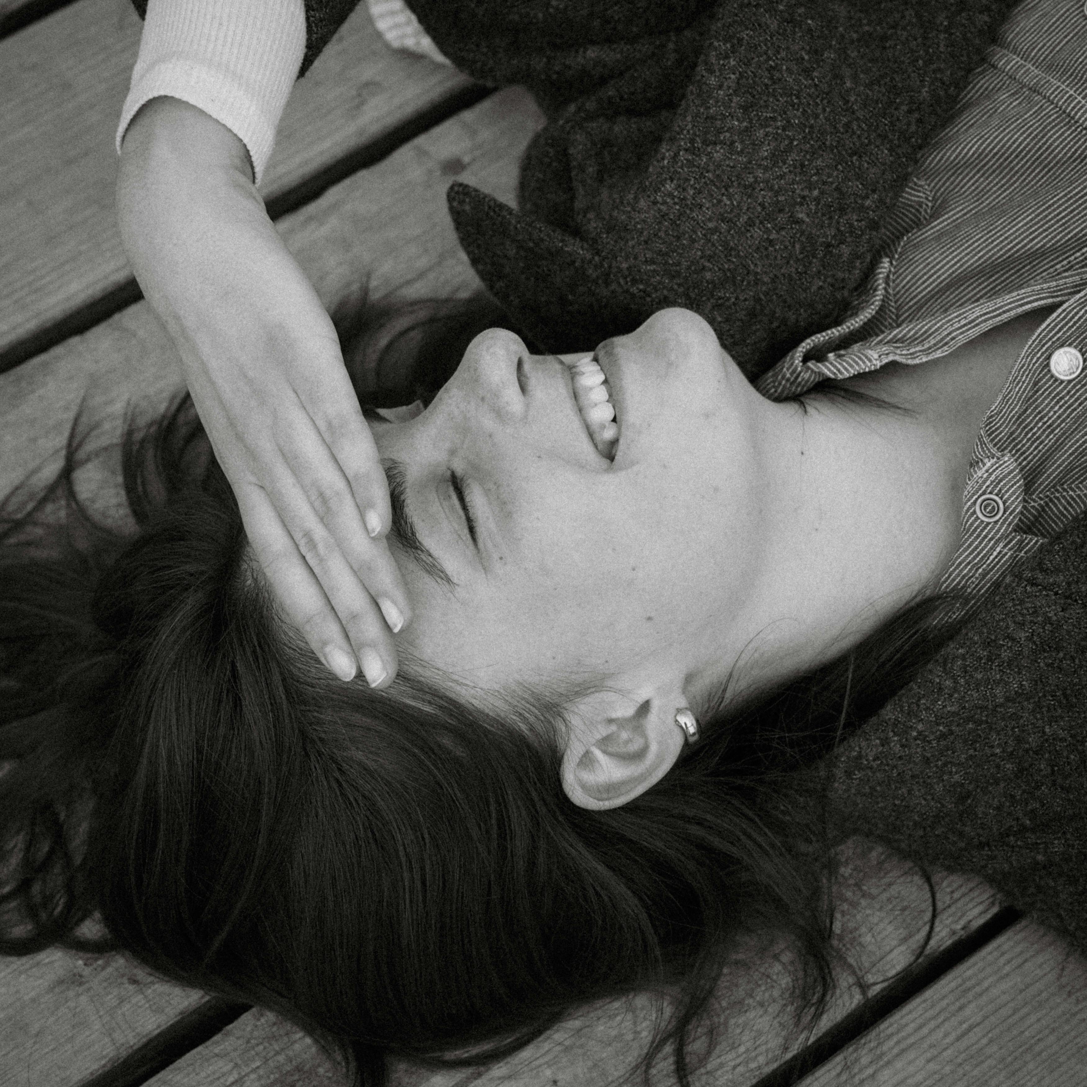 Black and white portrait of a young woman laughing while lying on a wooden deck.