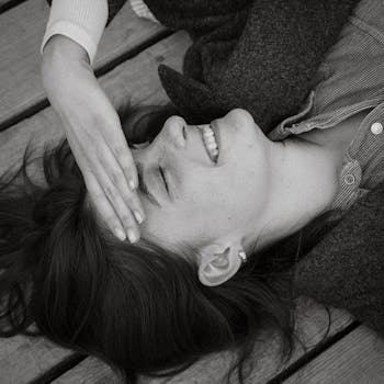 Black and white portrait of a young woman laughing while lying on a wooden deck.