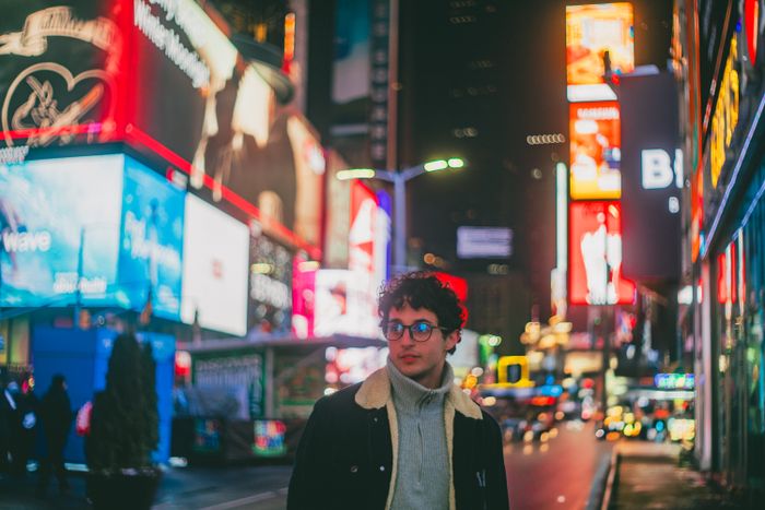 Young man in Times Square, New York City at night, surrounded by bright billboards and cit, by Renan Tagliaferro on Pexels