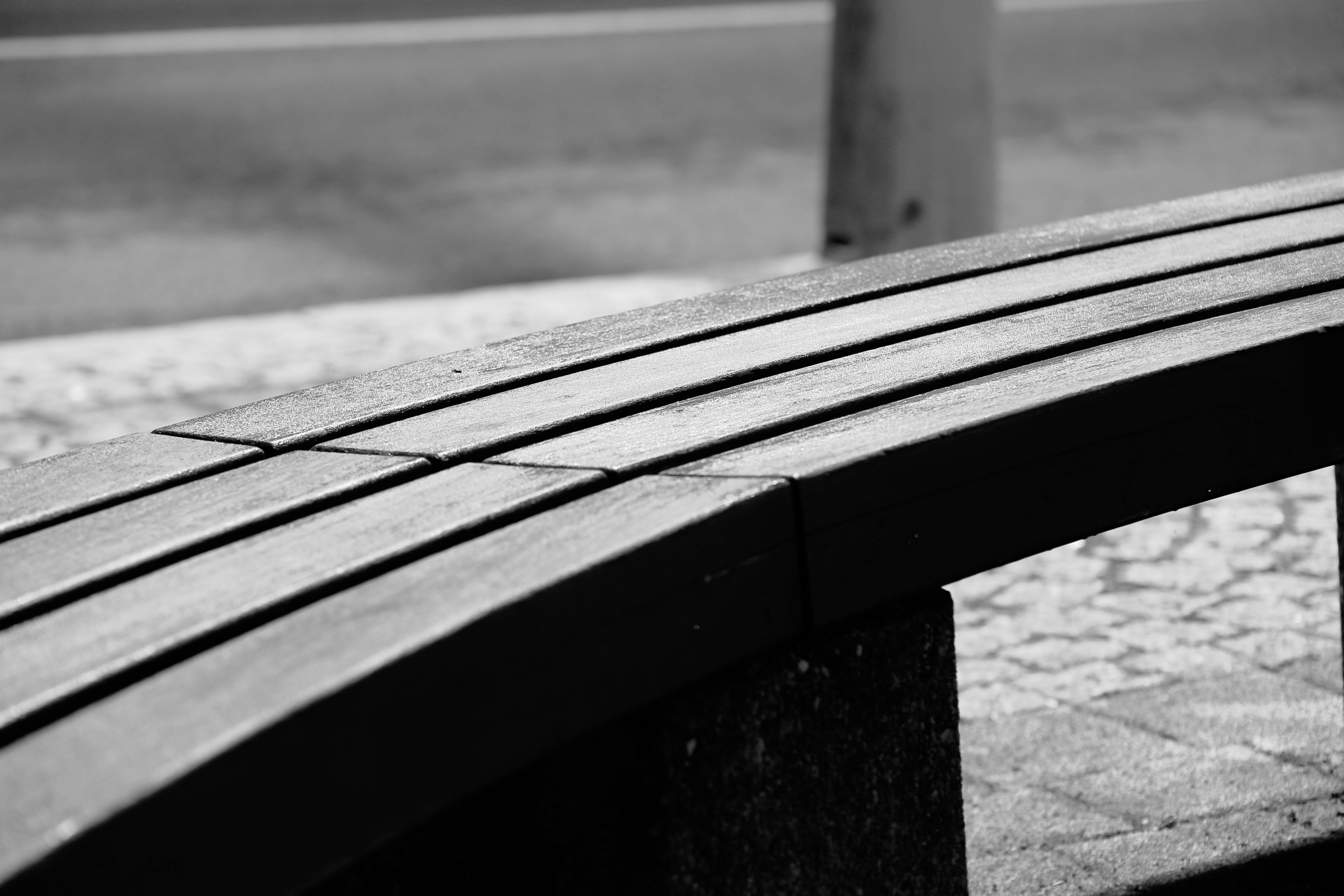 De franc Fotografia minimalista en blanc i negre d'un banc corbat de fusta en un entorn urbà. Foto d'estoc