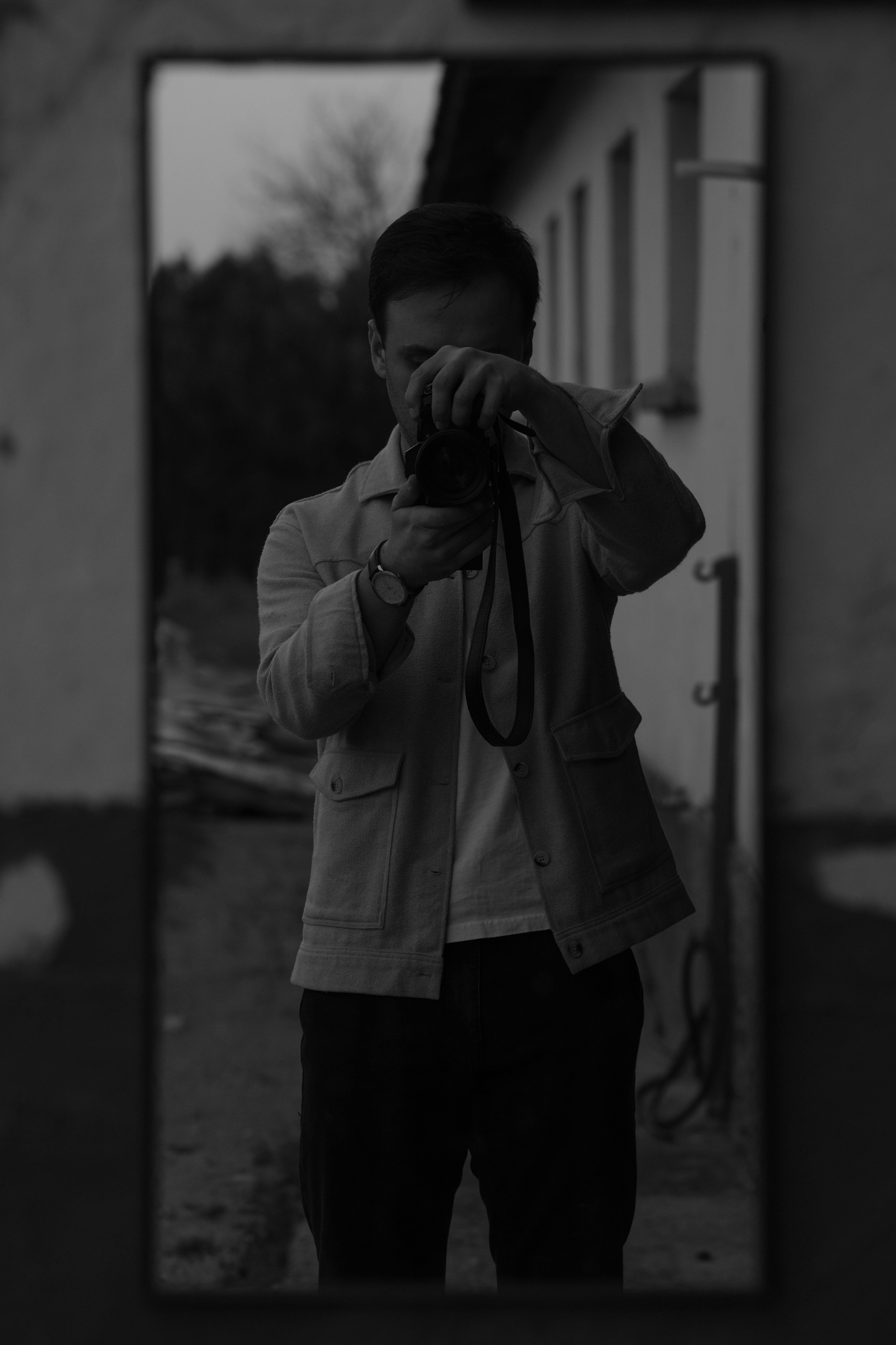 Monochrome image capturing a photographer's reflection in a mirror outdoors.