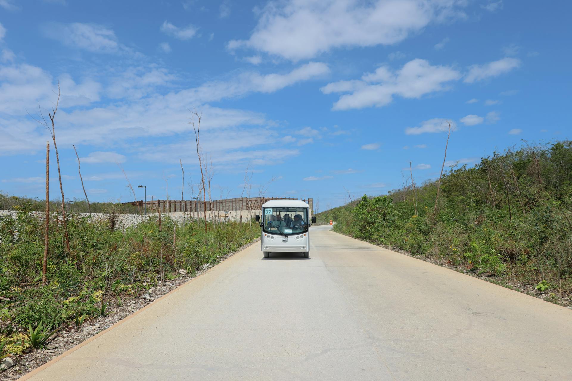 Electric shuttle bus on a sunny road in Tulum surrounded by nature and clear skies.