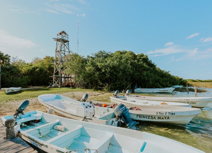 Small boats moored by a rustic observation tower on a sunny day, Tulum setting.