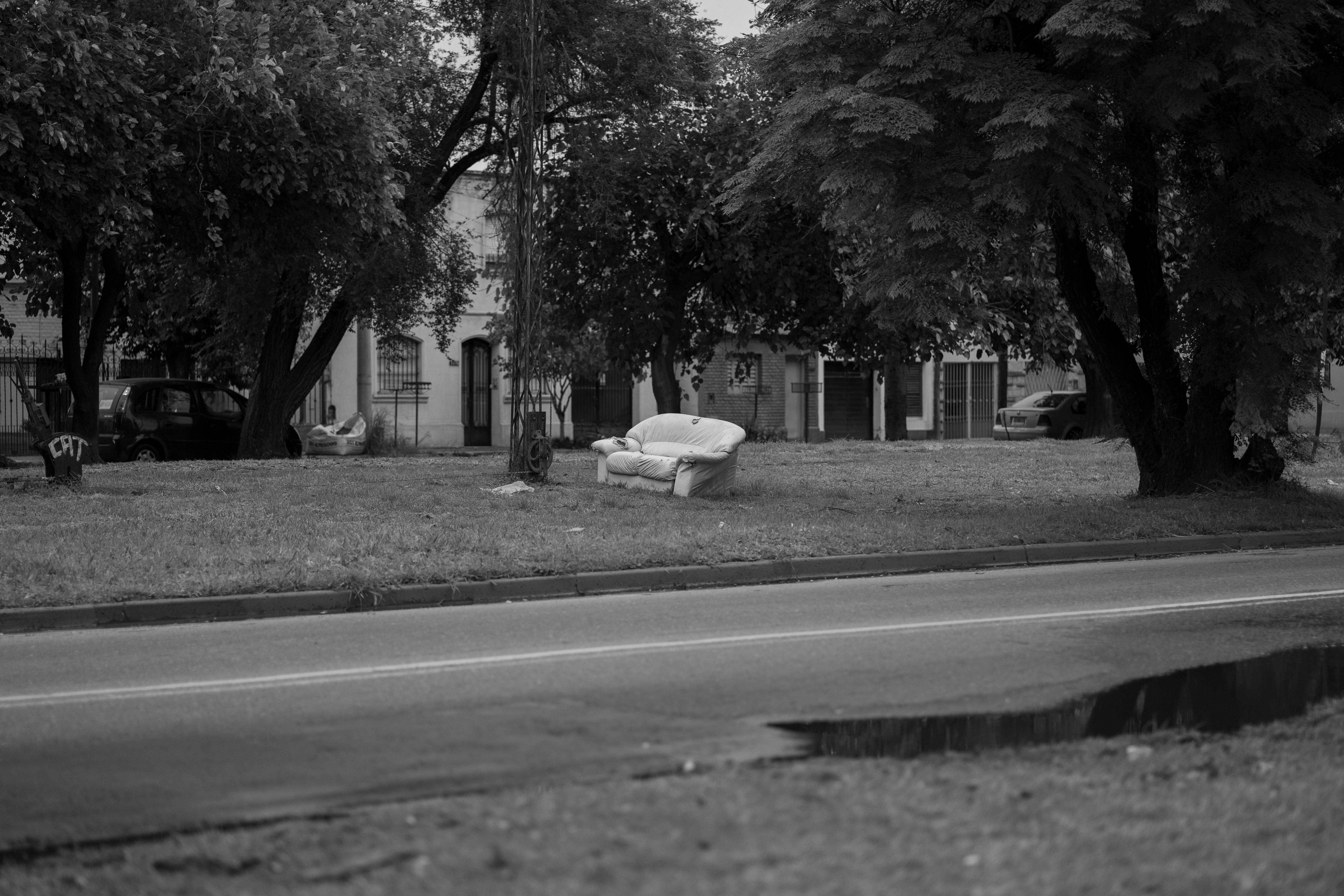 De franc Fotografia en blanc i negre d'una butaca abandonada en un carrer de Còrdova, Argentina, sota arbres frondosos. Foto d'estoc