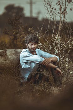 一位年轻人坐在户外，周围植被环绕，陷入沉思