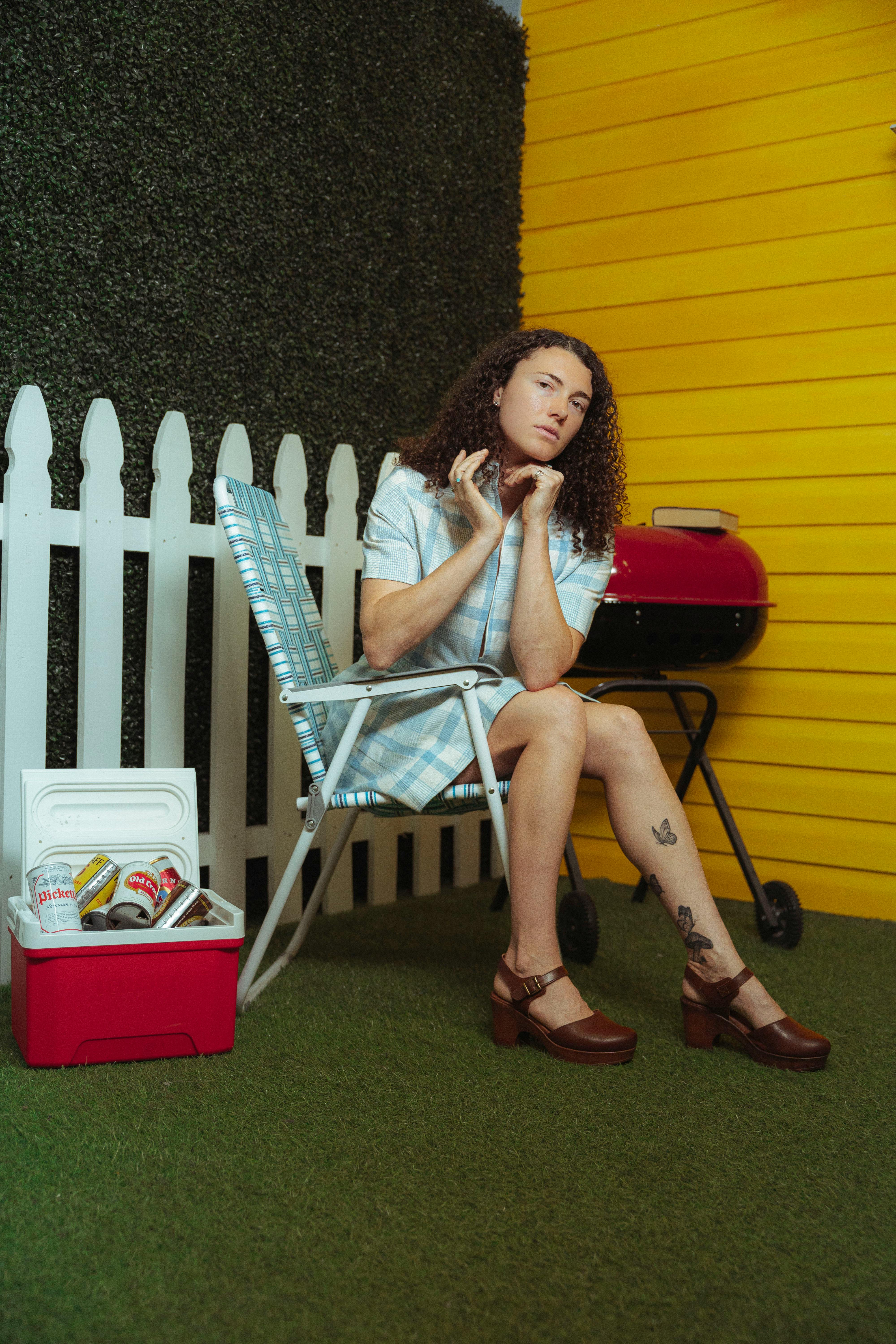 Woman sitting in a colorful retro backyard with a grill and cooler.