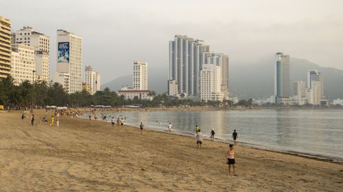 Free High-rise buildings line the serene beachfront as people enjoy a peaceful stroll along the coast. Stock Photo