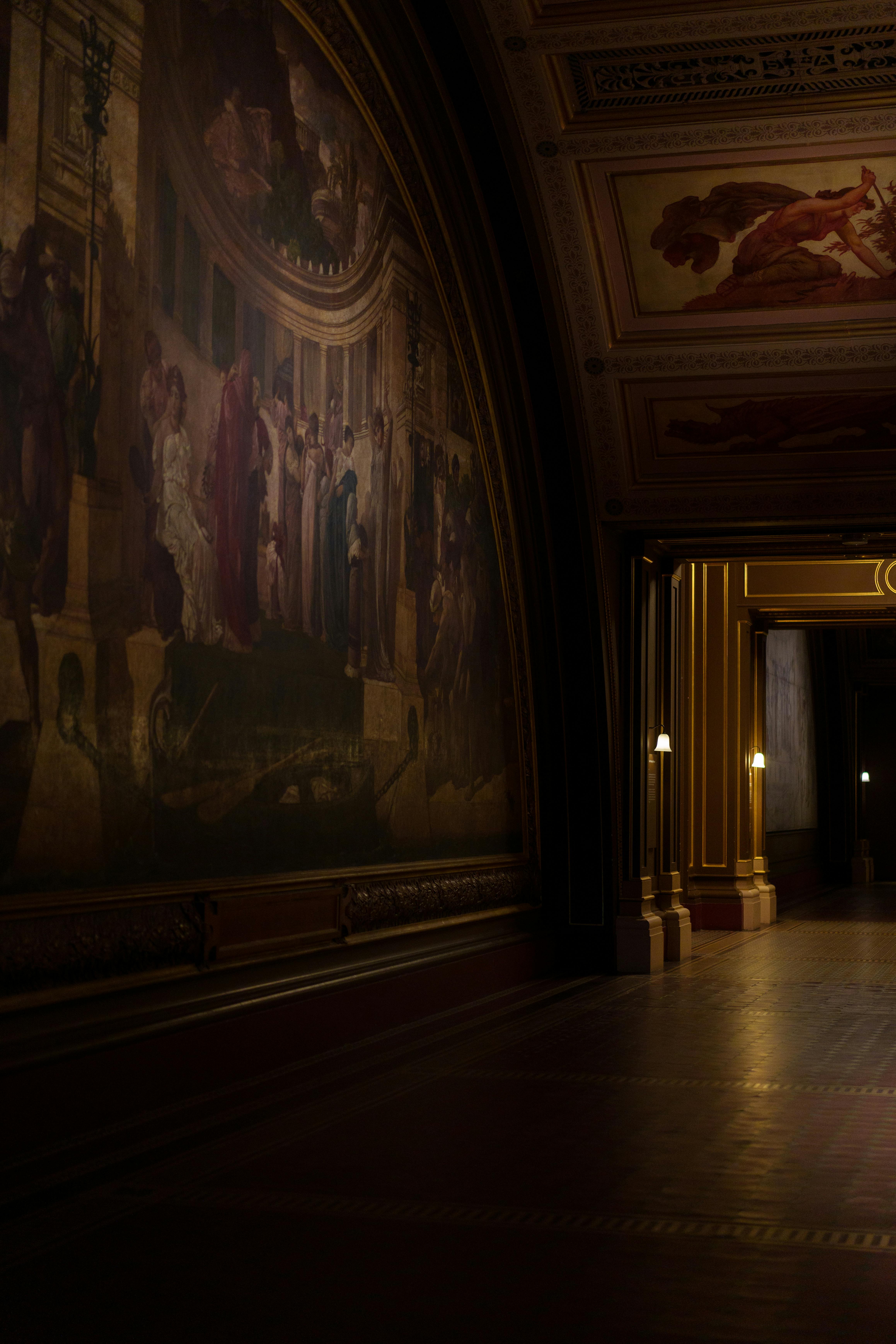 A dimly lit hallway with classic murals and elegant architecture.