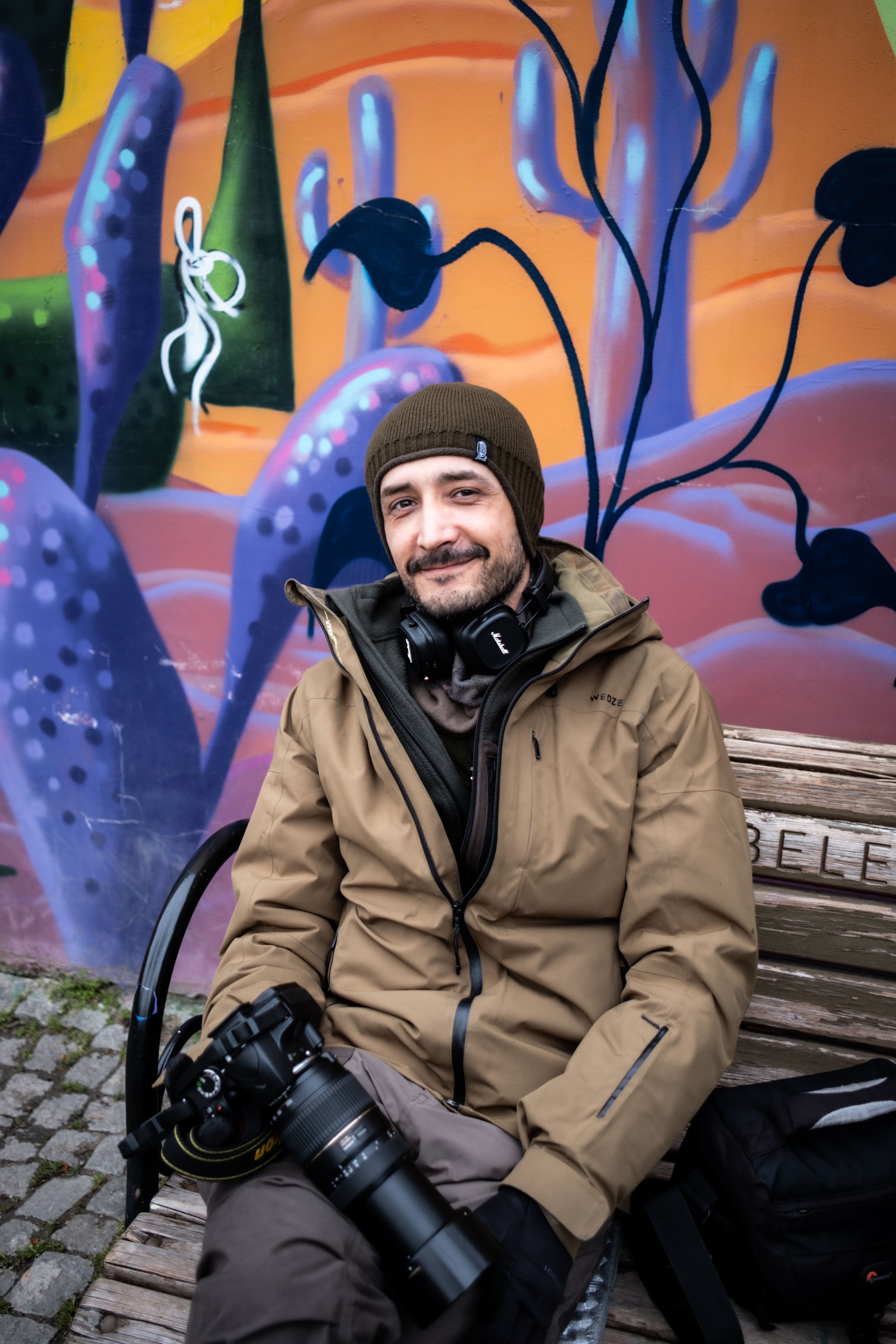 A photographer sits casually on a bench with his camera, against a colorful mural backdrop in Ankara, Türkiye.