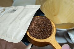 Wooden scoop with fresh coffee grounds being poured into a drip filter, ready for brewing.