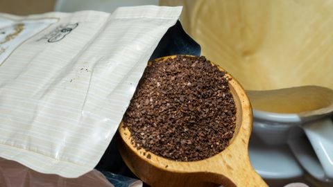 Wooden scoop with fresh coffee grounds being poured into a drip filter, ready for brewing.