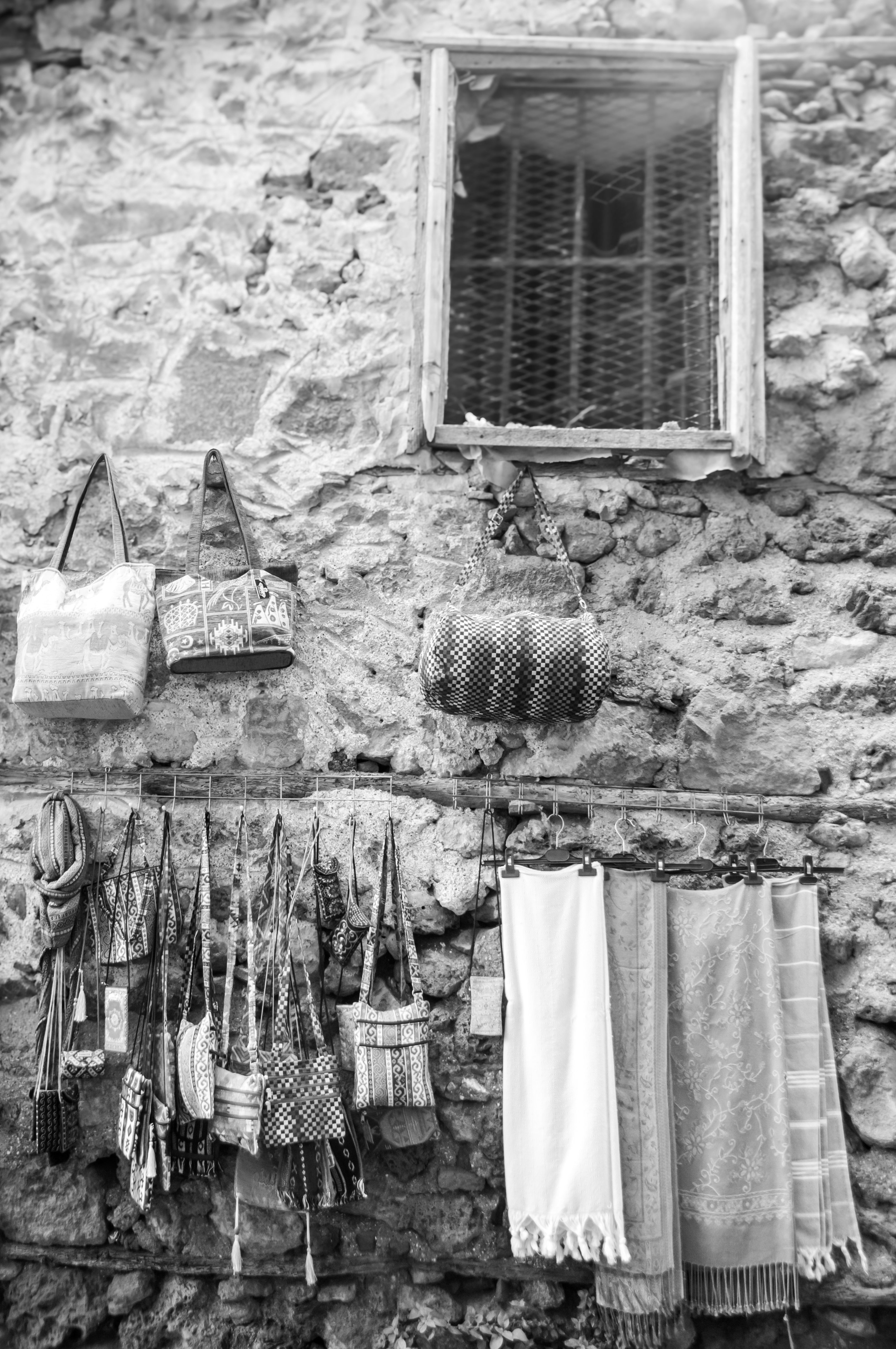 A rustic display of bags and textiles on a stone wall, featuring handcrafted designs in a quaint outdoor setting.