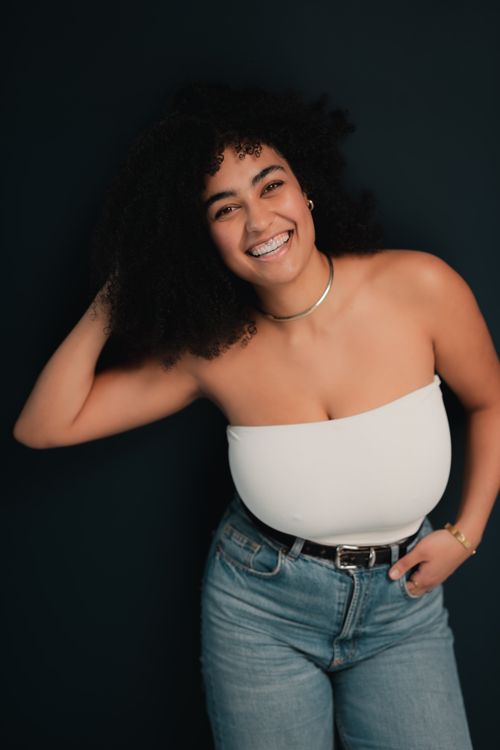 Free Cheerful young woman with curly hair posing confidently against a dark background. Stock Photo
