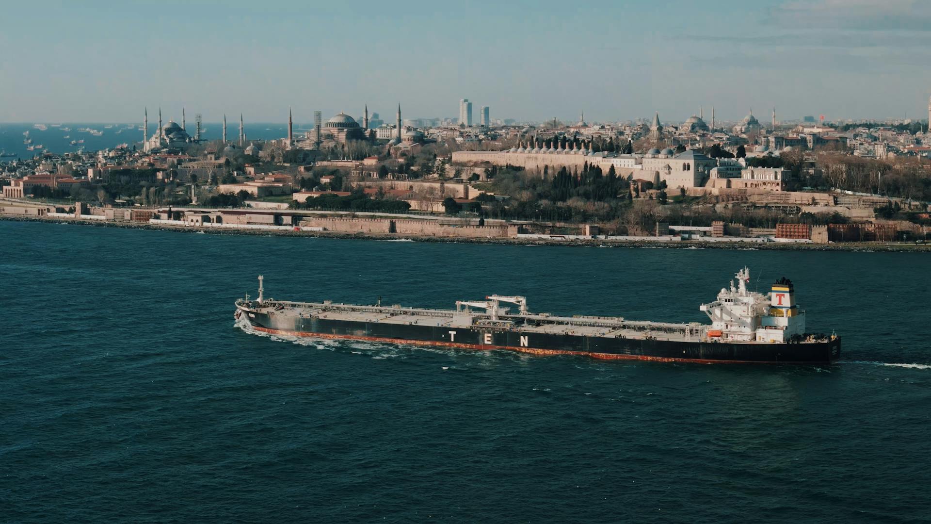 Aerial shot of a cargo ship sailing through the Bosphorus with Istanbul's historic skyline in the background.