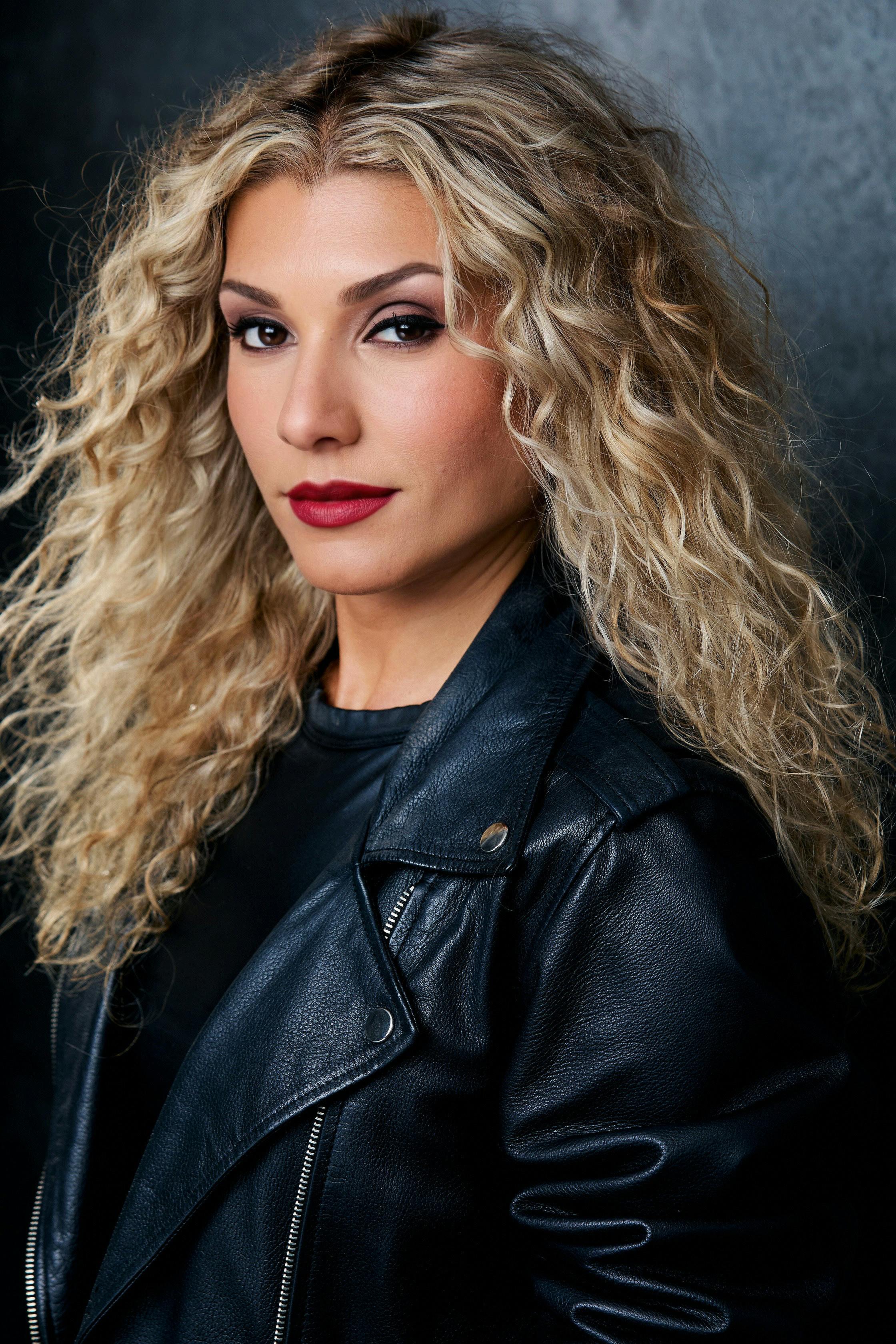 Stylish woman with curly hair and leather jacket in studio.