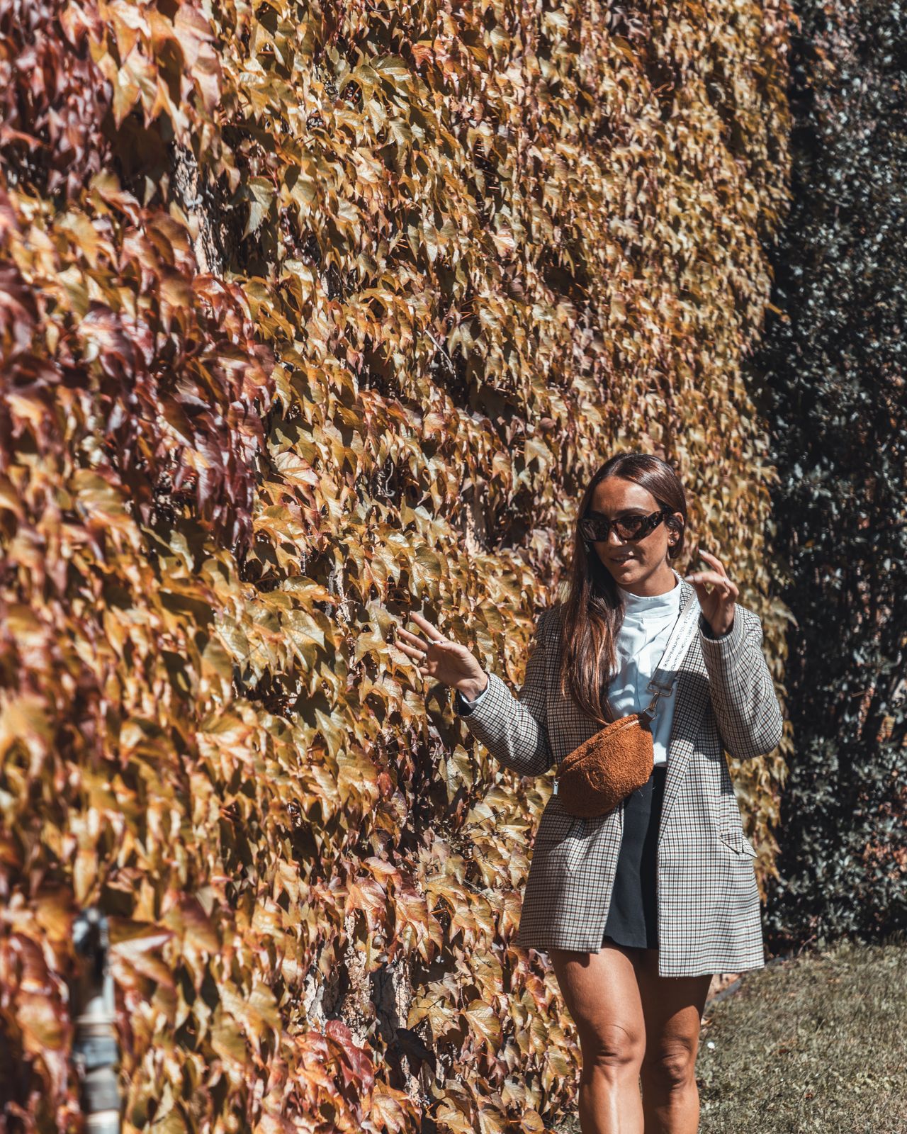 Woman in a gray coat standing against a wall of autumn ivy