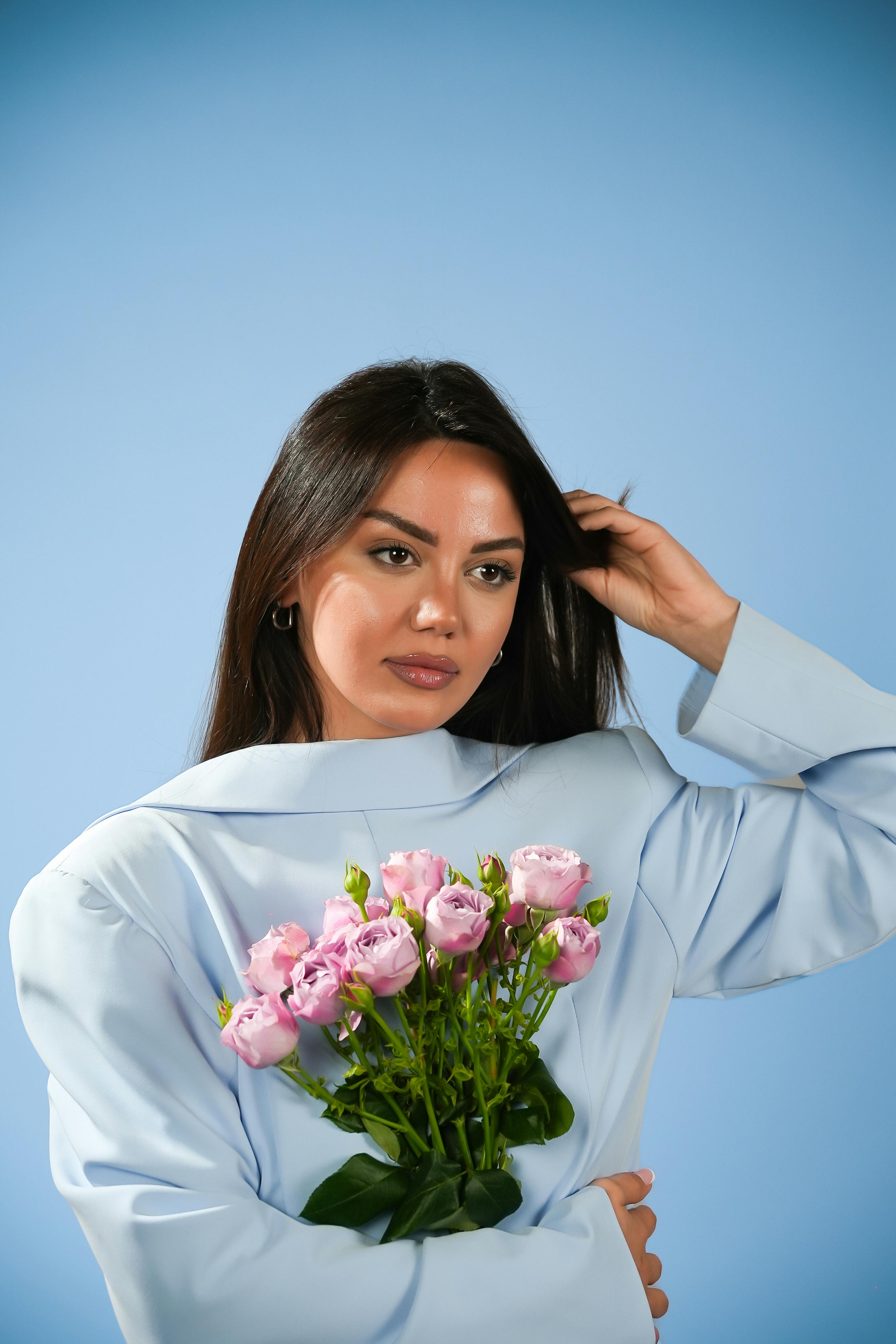 Miễn phí Người phụ nữ sành điệu trong trang phục màu xanh với hoa hồng màu hồng trong bối cảnh studio. Lý tưởng cho chủ đề thời trang và phong cách sống. Ảnh lưu trữ