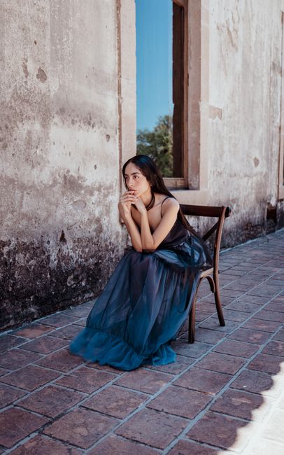 Young woman in a flowing blue dress sitting outside in Le贸n, Mexico.