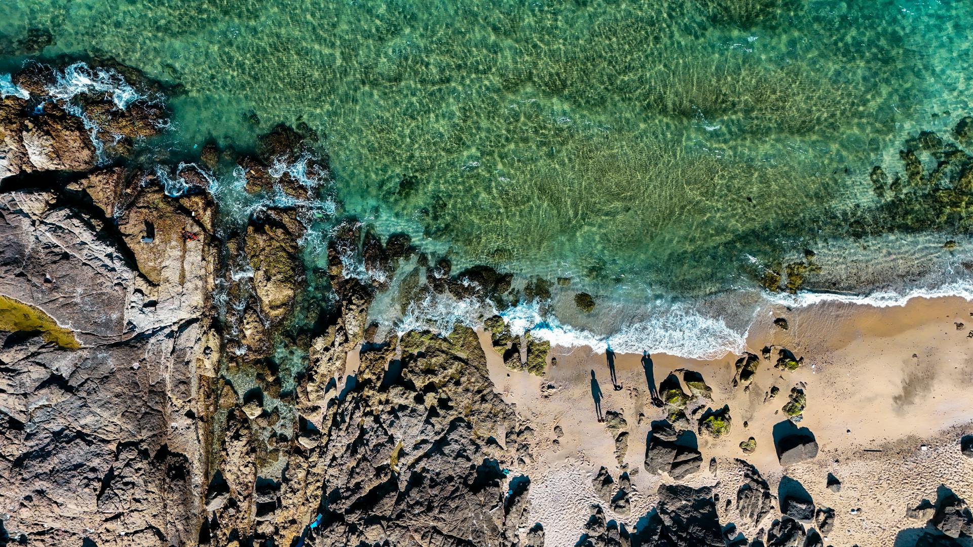 Stunning aerial shot of rocky coastline with clear turquoise waters and sandy beach.