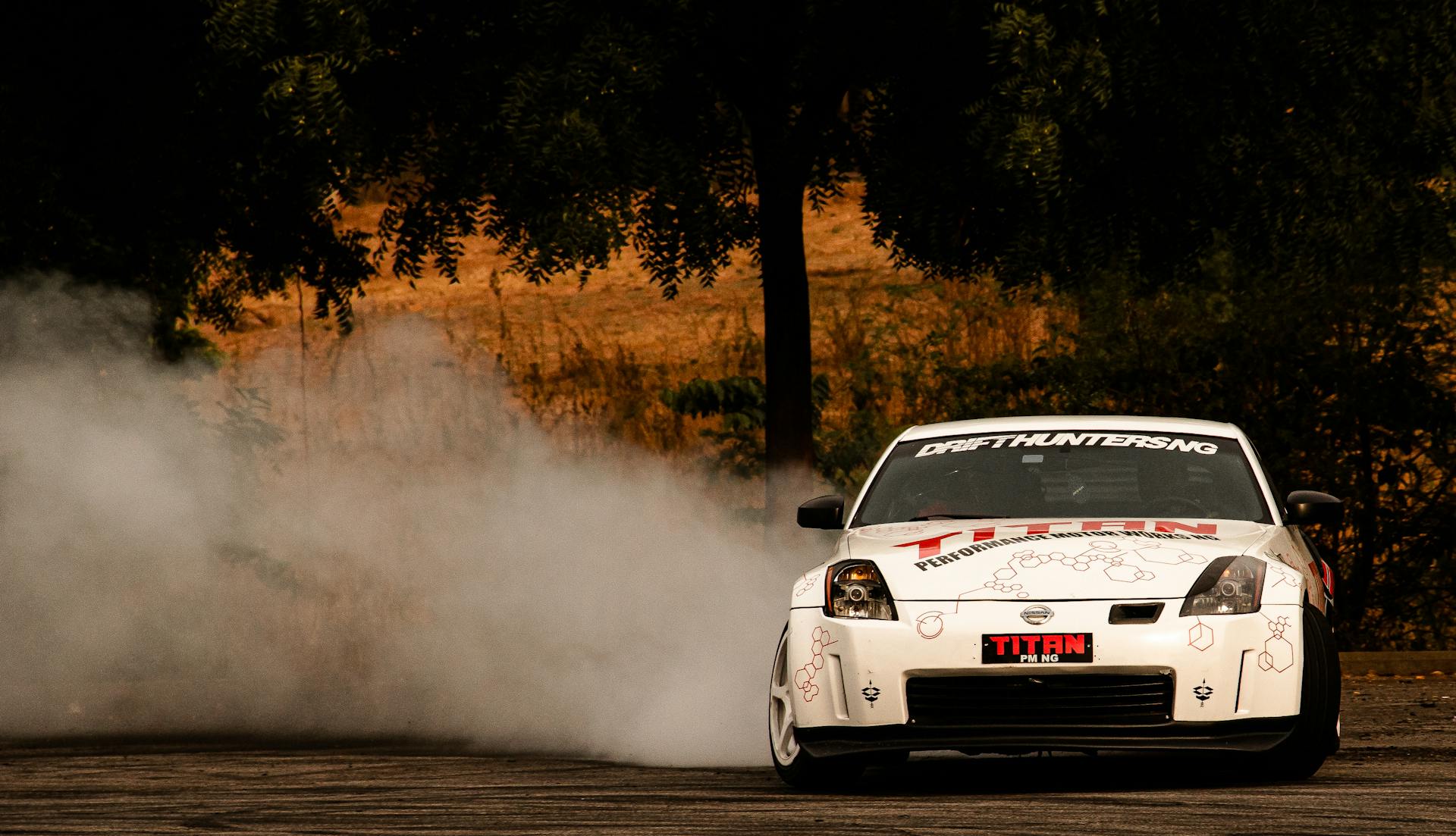 White drift car skidding on track, creating smoke in scenic outdoor setting.