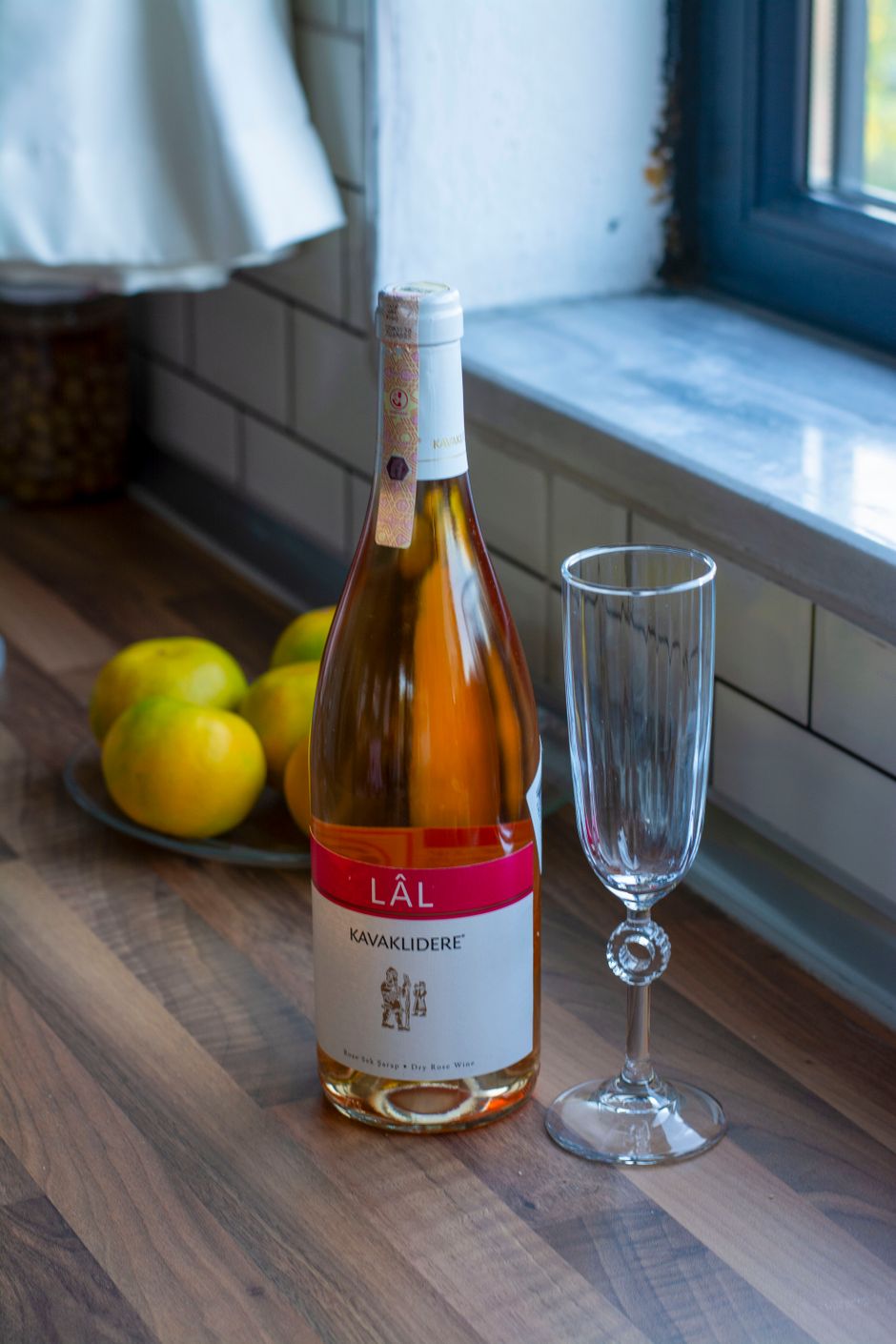 A bottle of Kavaklidere Lal wine beside a glass on a wooden kitchen counter.