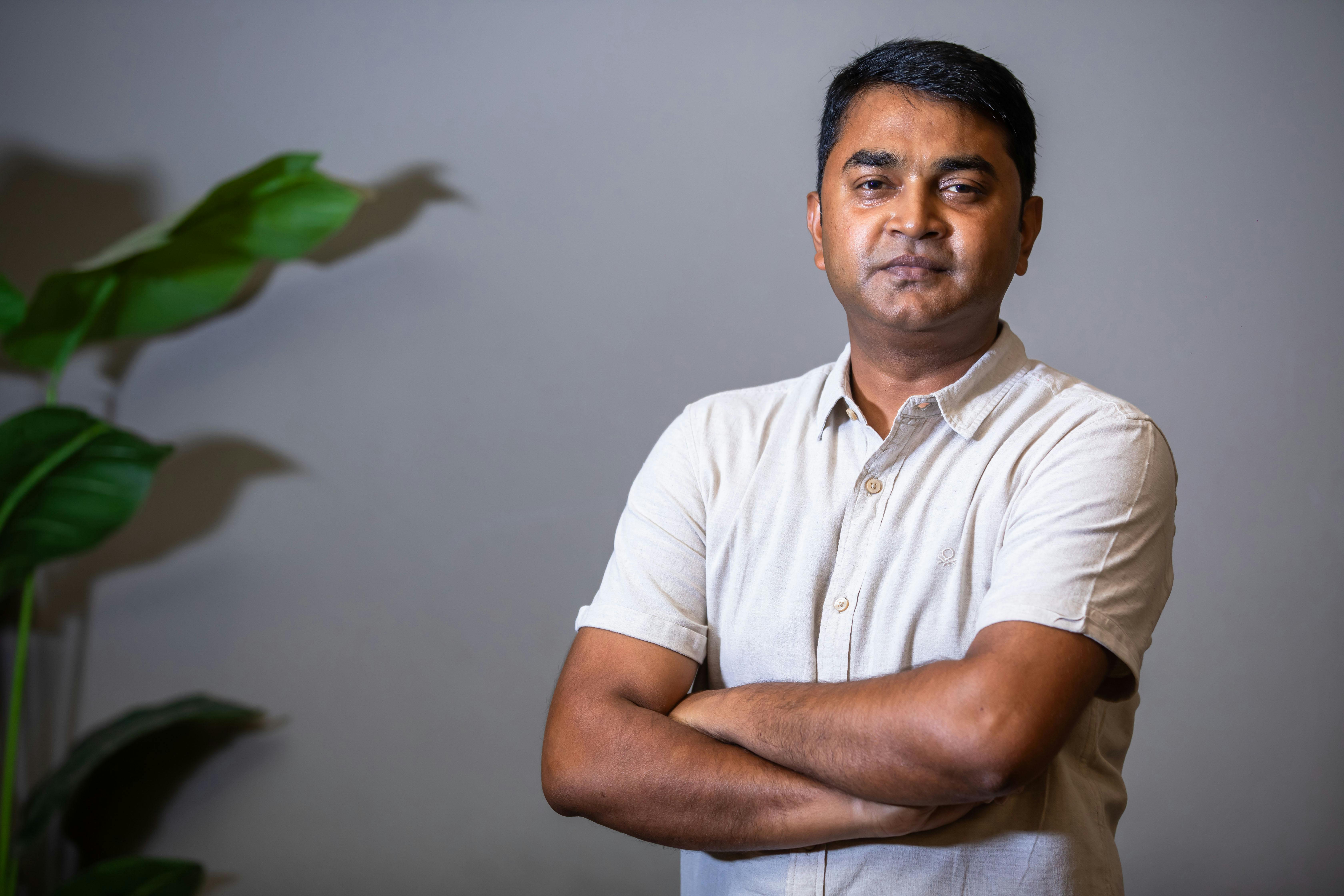 Portrait of a confident adult man with arms crossed, standing in a well-lit indoor setting.