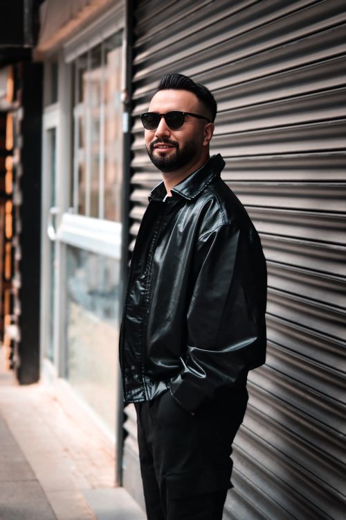 Free Confident man in black leather jacket and sunglasses posing against urban backdrop. Stock Photo