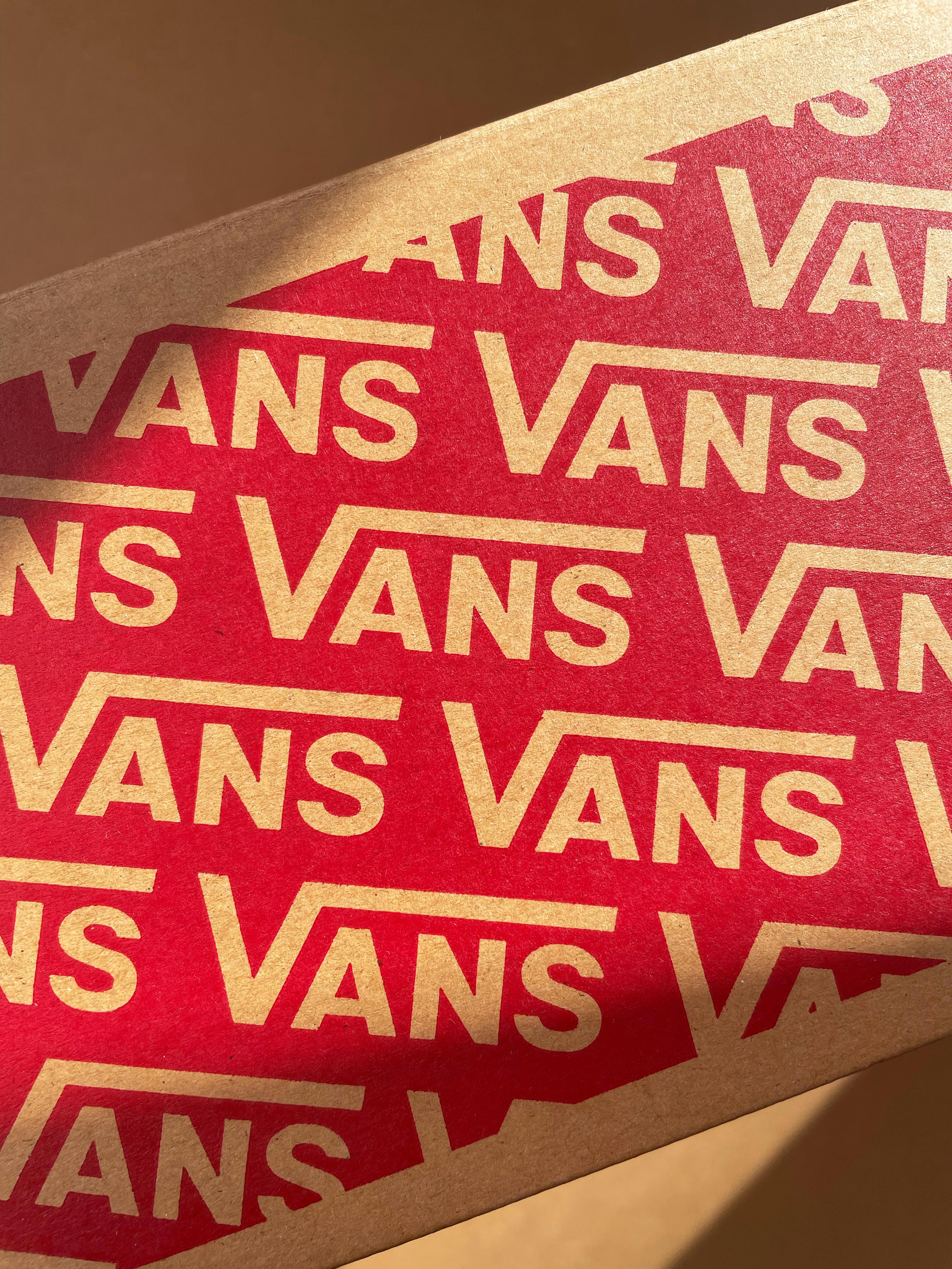 Close-up of Vans logo on a red and brown cardboard box, daylight.