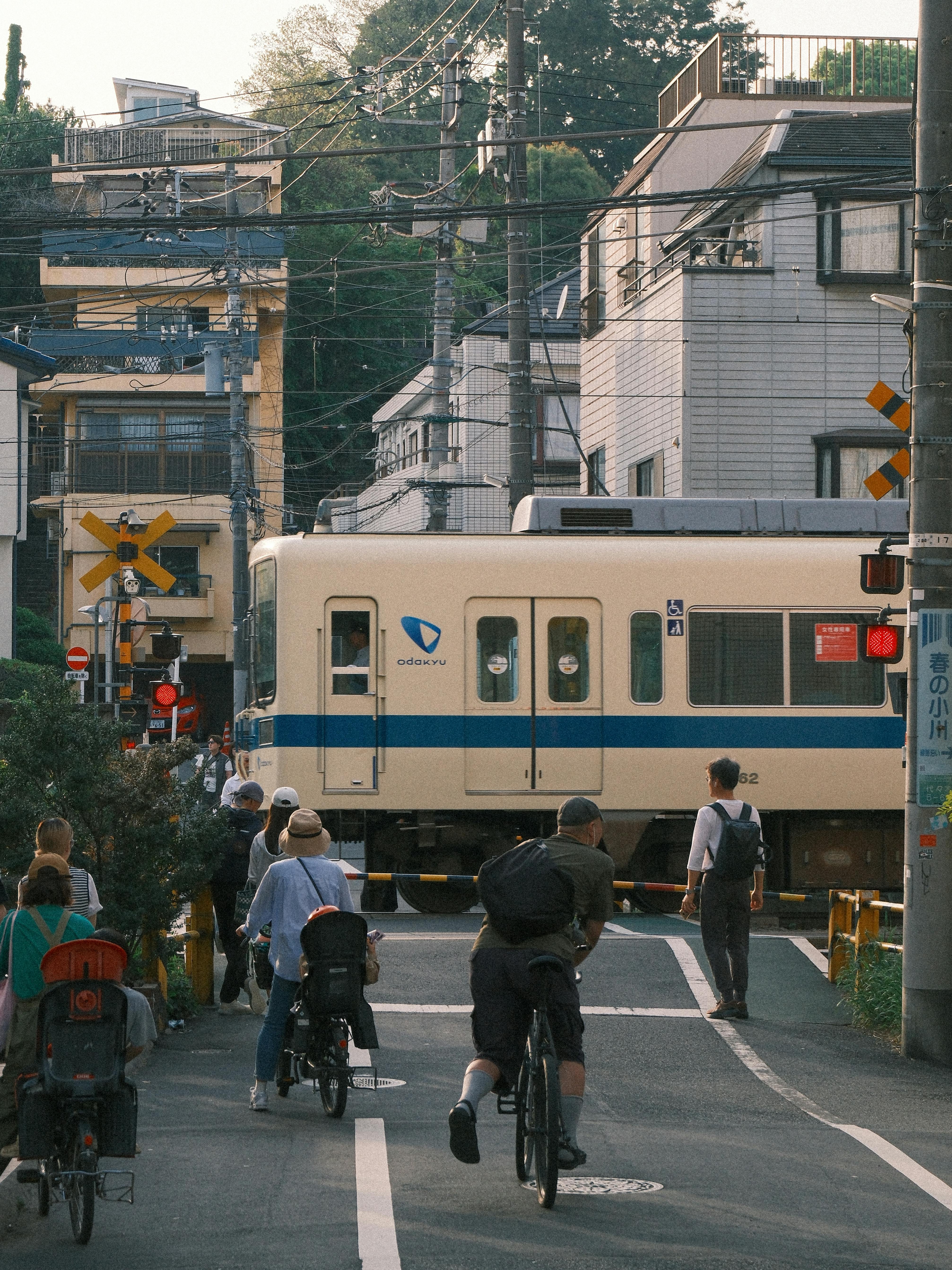A lively Tokyo street scene with pedestrians and cyclists waiting as a train passes by.