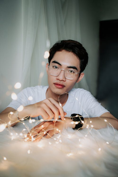 Free Man Wearing White Crew-neck T-shirt Sitting Near String Lights Stock Photo