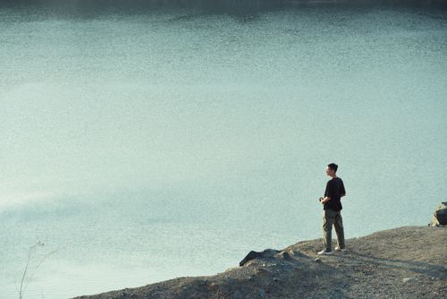 Free Solo man stands on rocky shore, gazing at serene lake view. Stock Photo