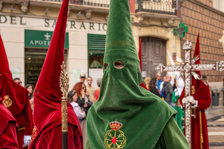 Colorida procesión tradicional de Semana Santa con participantes encapuchados en Málaga, España.