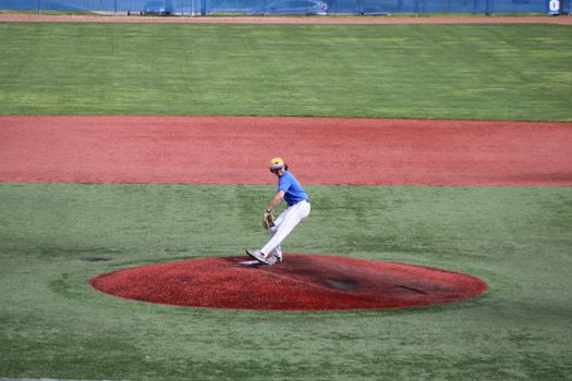 Teenage baseball pitcher throws a ball on an outdoor field, showcasing athletic skill.