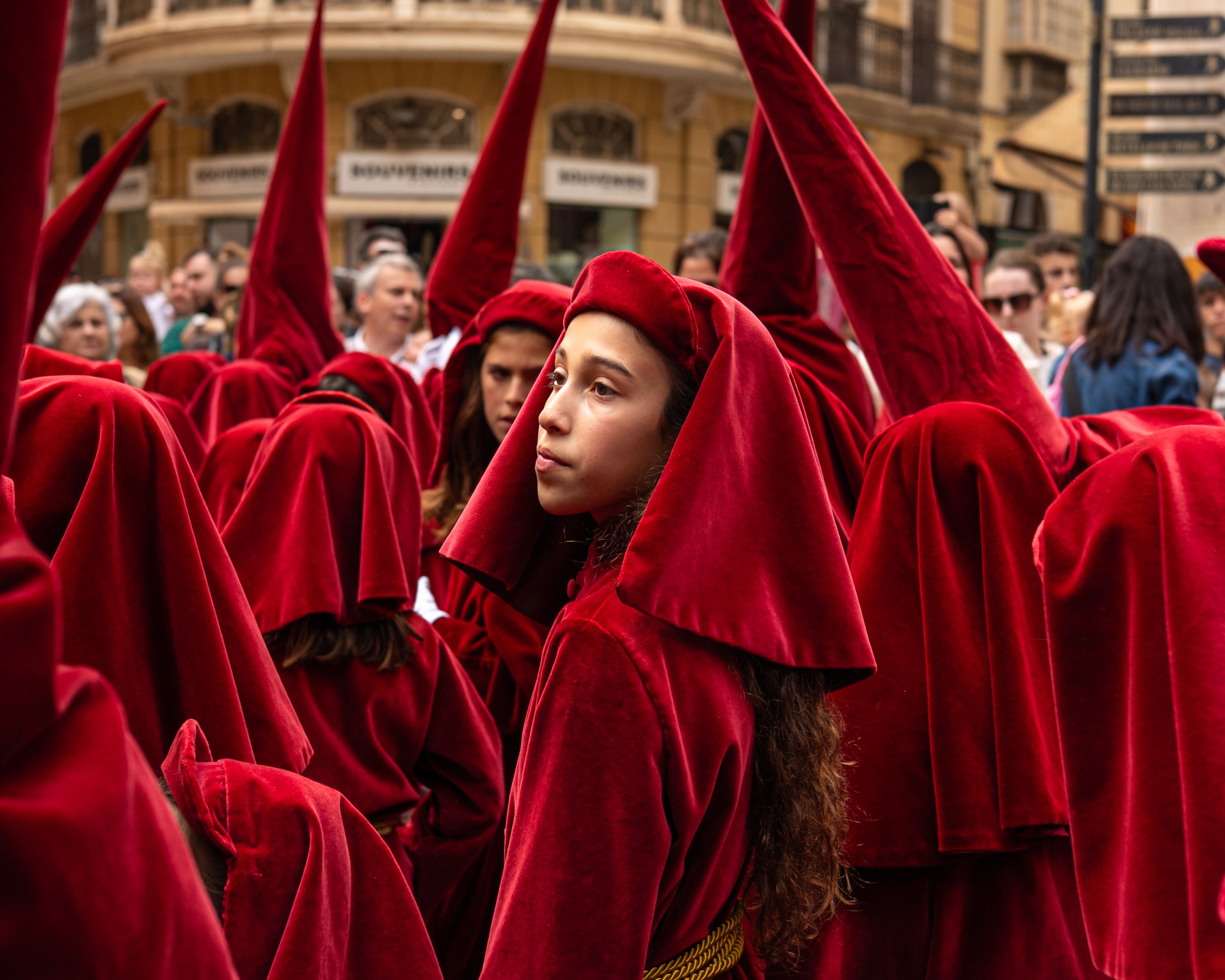 A solemn religious procession with penitents walking through a Spanish city street.