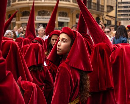 Young participants in red robes during a religious procession in Málaga, Spain.