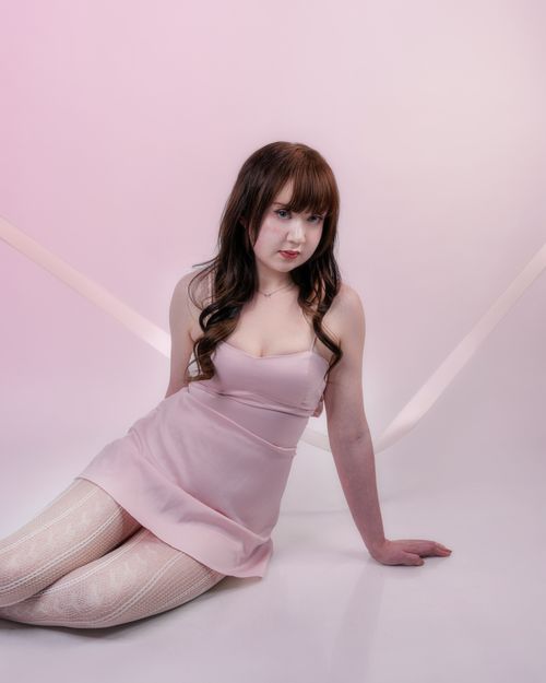 Free Charming portrait of a woman sitting gracefully in a soft pink dress against a pastel background. Stock Photo