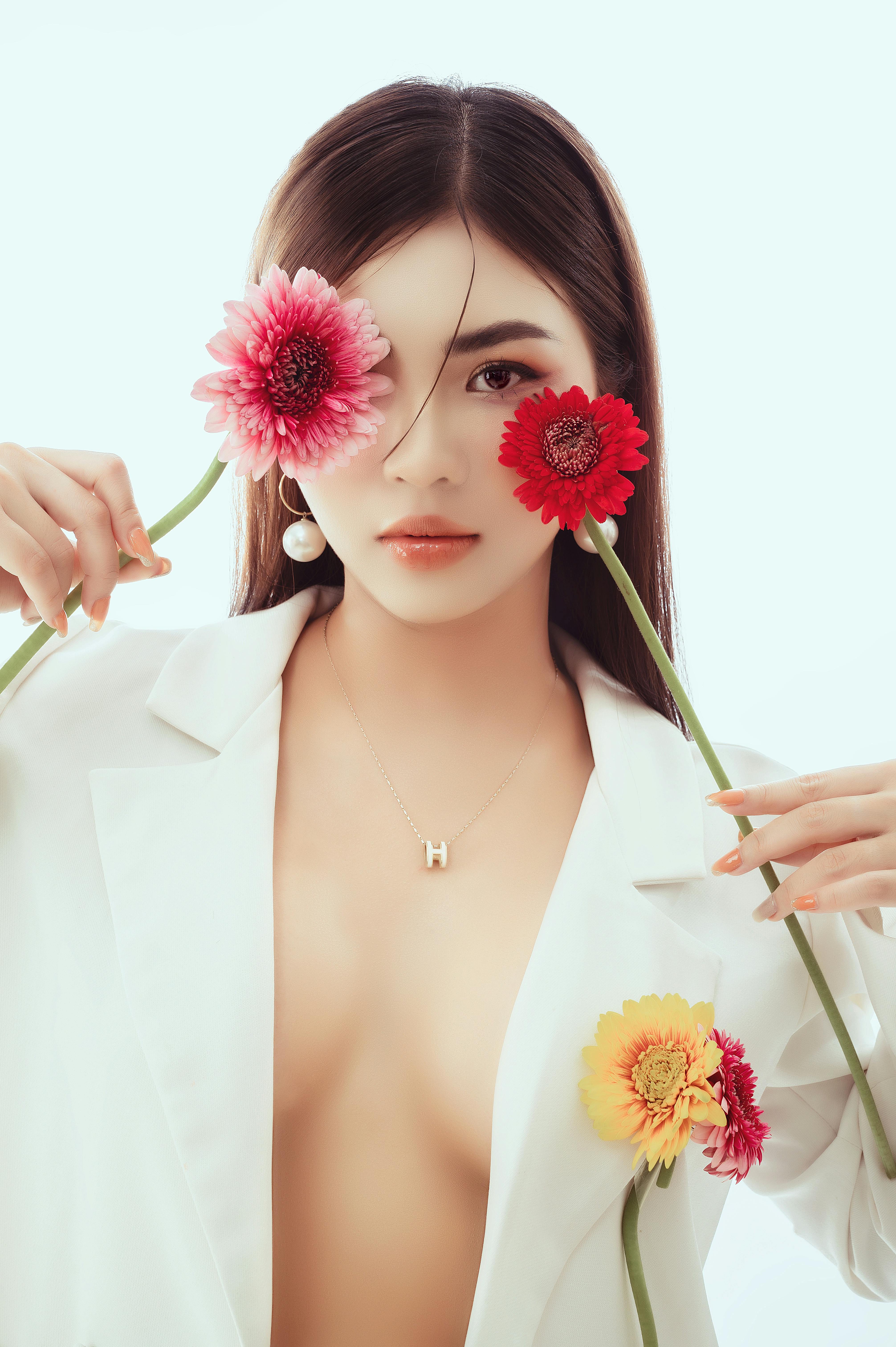Woman in white blazer posing with gerbera flowers, combining elegance and floral art.