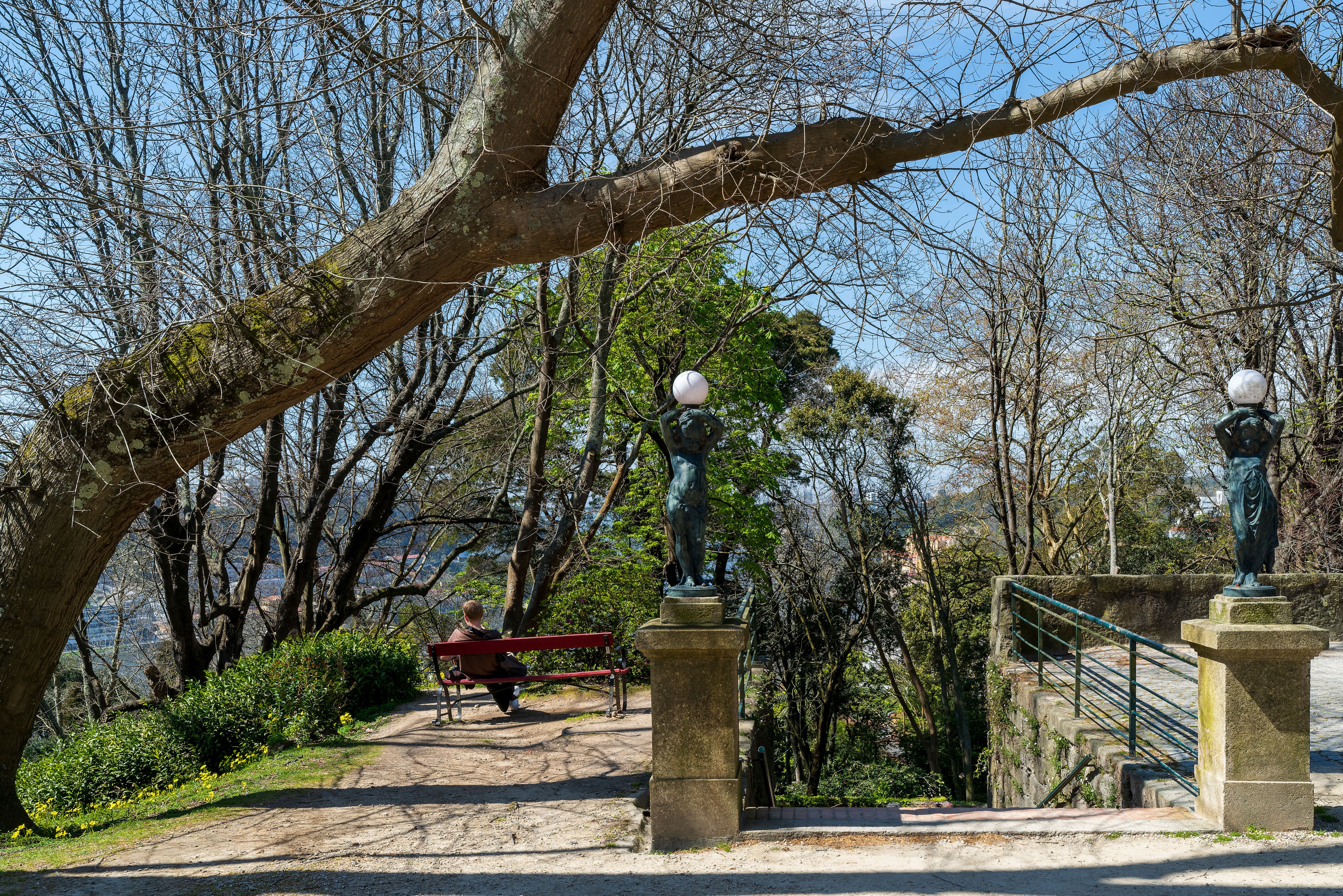 A tranquil park scene in Porto, Portugal, featuring bronze statues and a peaceful bench under trees.